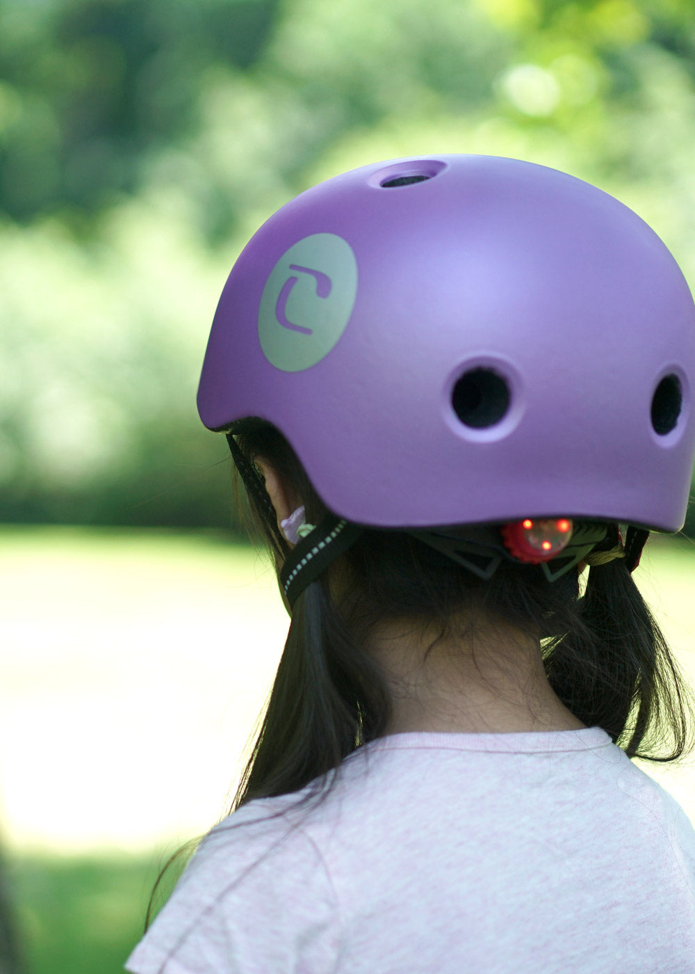 Little girl wearing a lilac helmet showing off the safety light features on the adjustable twist dial