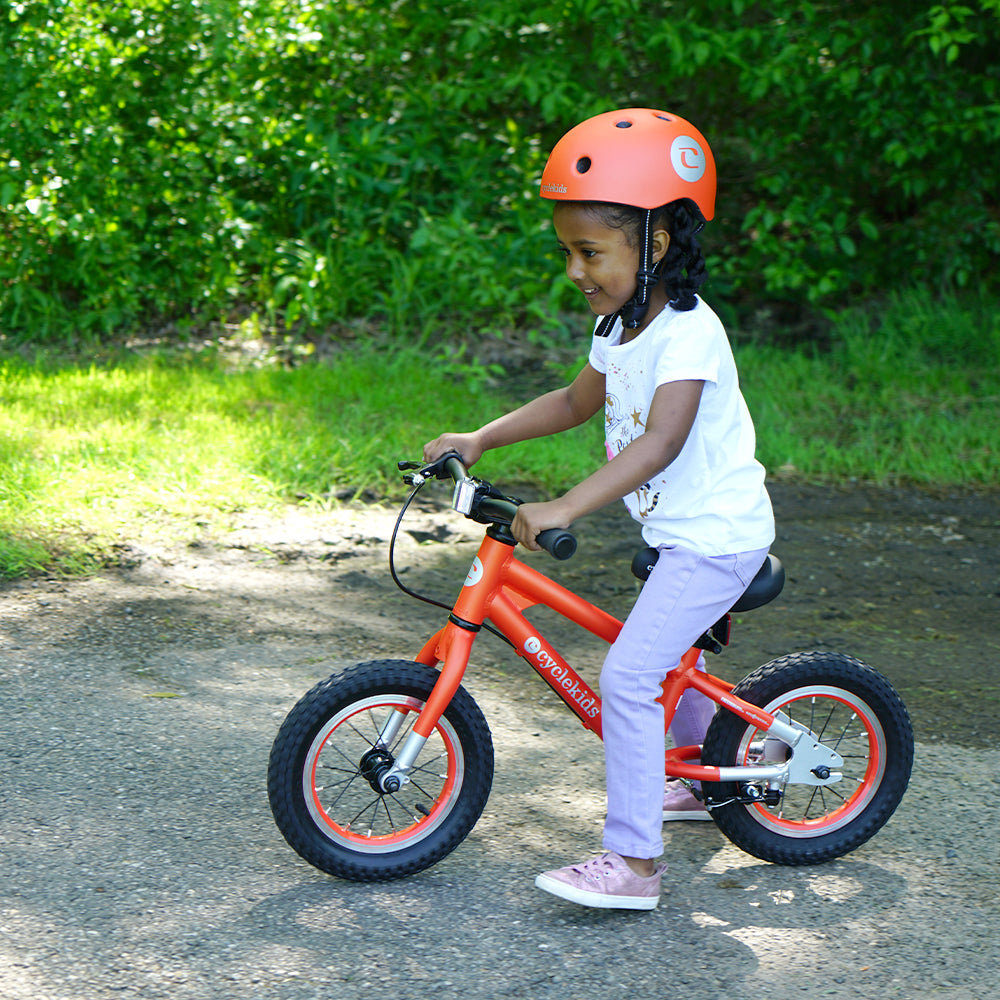 Little girl on a 12" CYCLEKids Balance bike in orange and her matching helmet