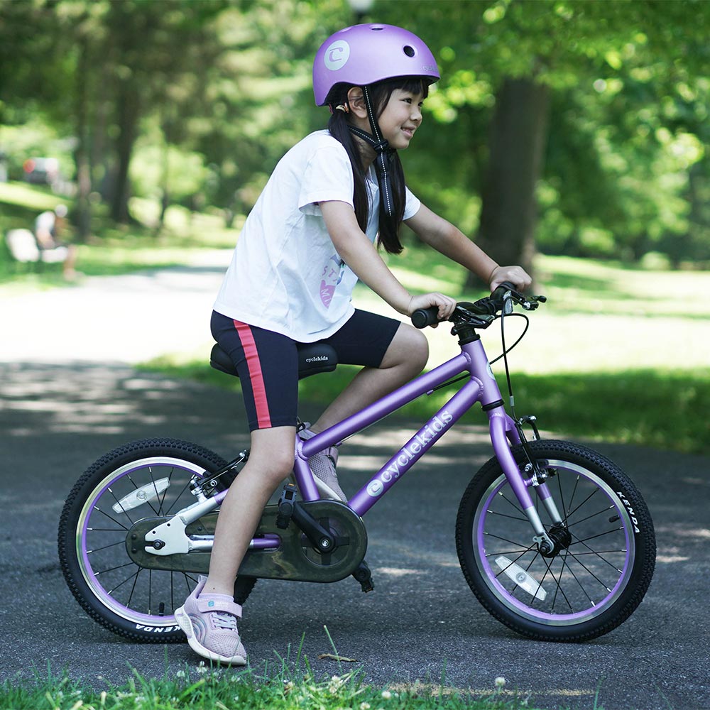 Little asian girl with her 16" CYCLEKids bike in lilac with her matching helmet pushing off the ground getting ready to ride
