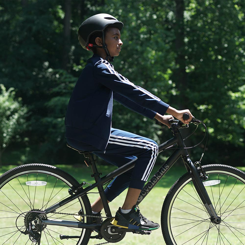 A pre-teen boy riding with his 26" CYCLEKids Bike in black and a matching helmet