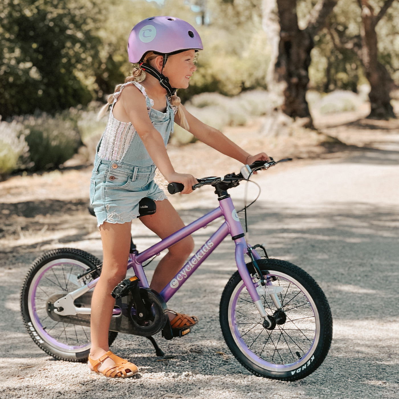 A little blonde girl standing with her 16" CYCLEKids bike in lilac and a matching helmet