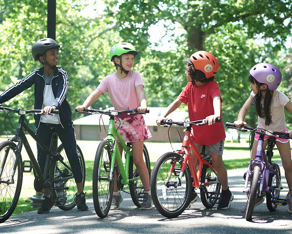 A lineup of kids standing side by side with their 12" to 26" CYCLEKids Bikes and matching helmets