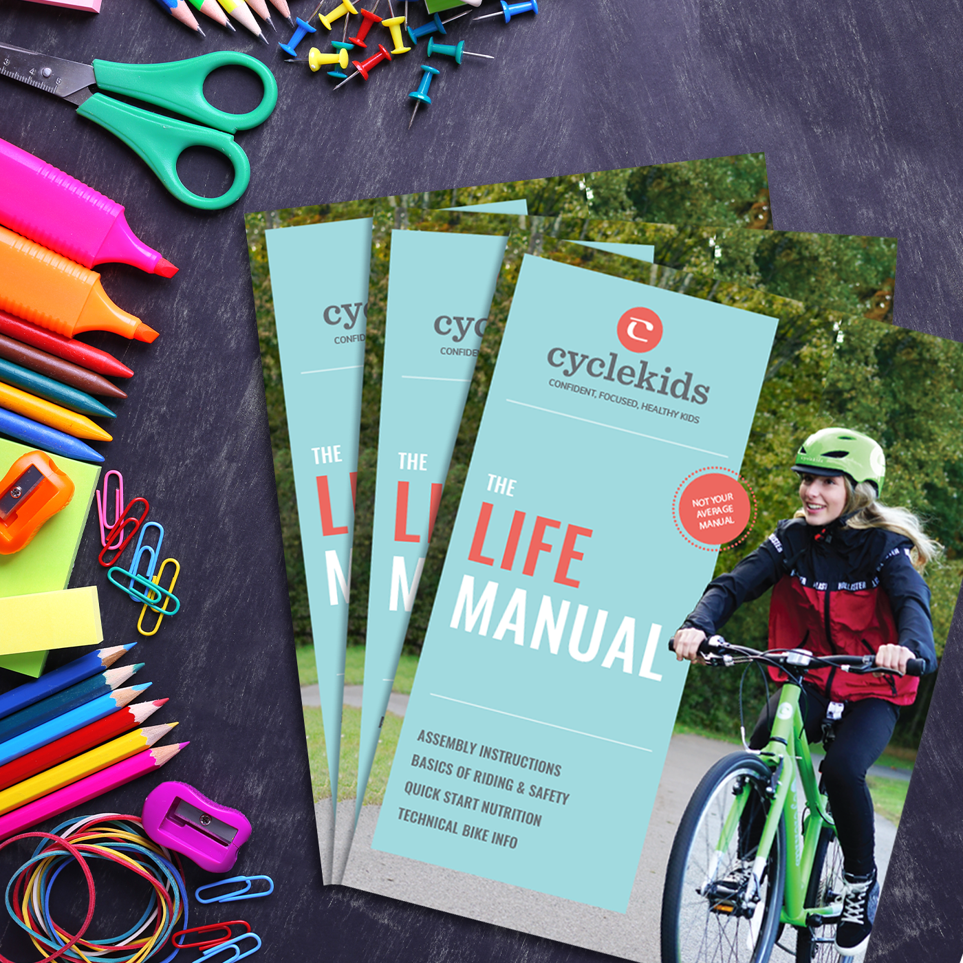 The CYCLEKids bike Life Manuals on a table with colorful kid school supplies